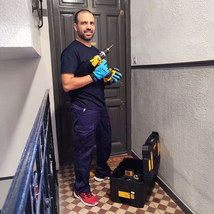 Persona con cinturón de herramientas instalando una manija en una puerta blanca.