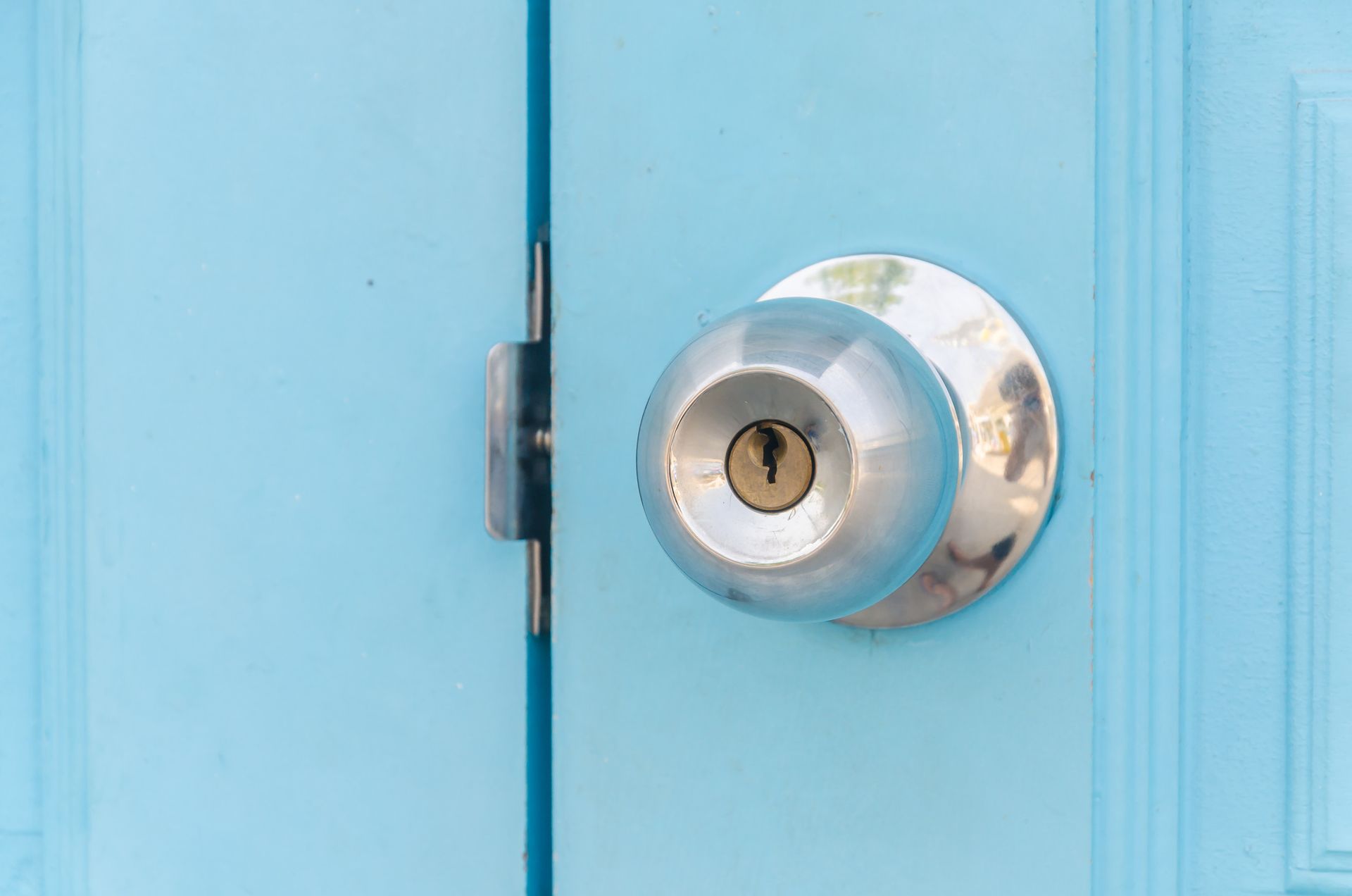 Pomo de puerta plateado en una puerta azul claro con una llave en la cerradura.