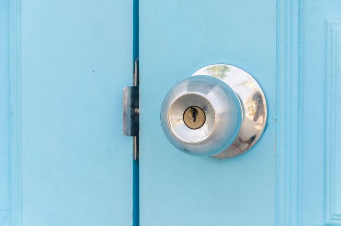 Pomo de puerta plateado en una puerta azul claro con una llave en la cerradura.
