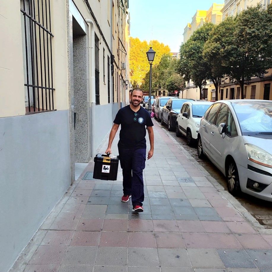 Un manitas usa un taladro para instalar herrajes en una puerta blanca. Lleva un cinturón de herramientas y está de pie en el interior.