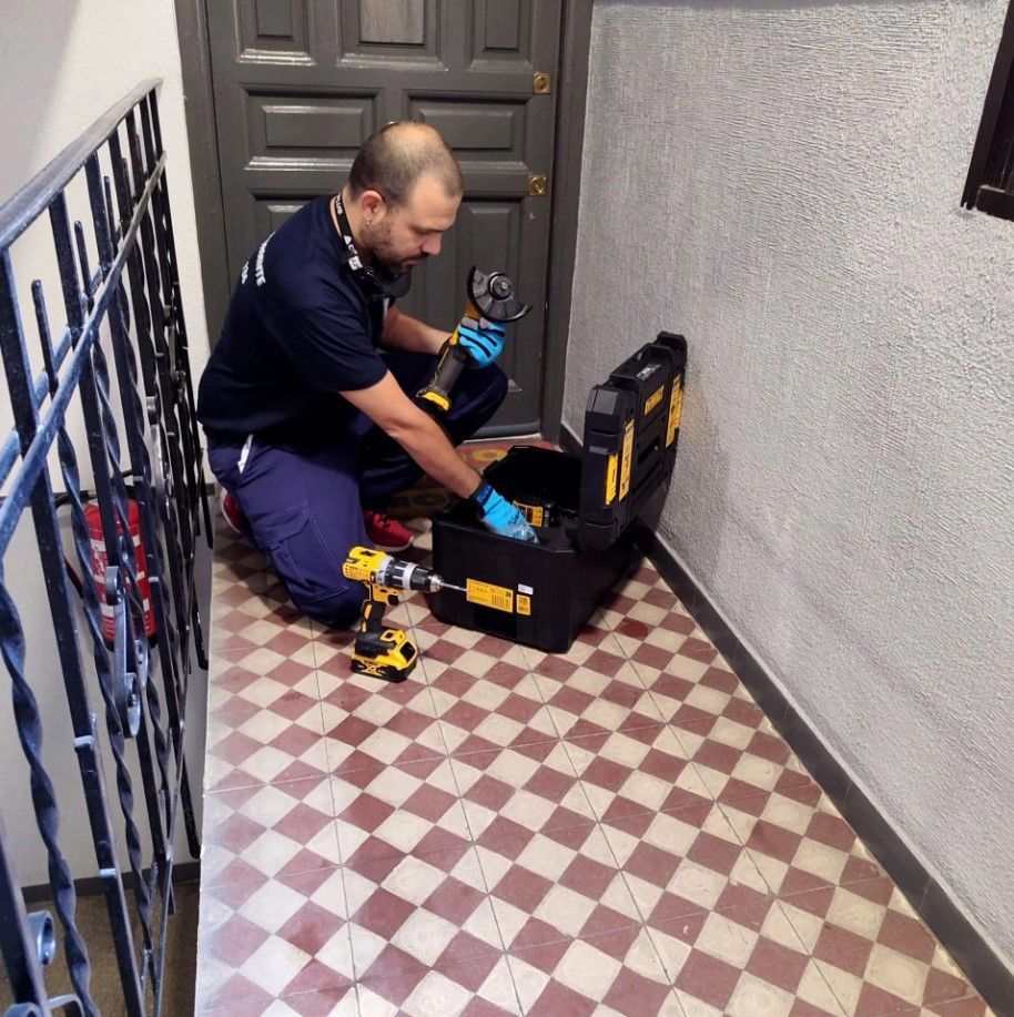 Un manitas usa un taladro para instalar herrajes en una puerta blanca. Lleva un cinturón de herramientas y está de pie en el interior.