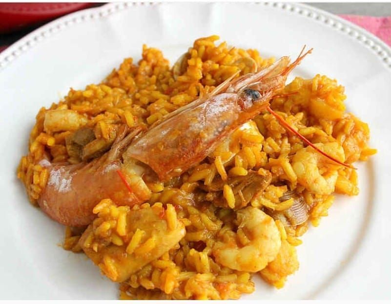 Paella con camarones en plato blanco; arroz dorado con mariscos.