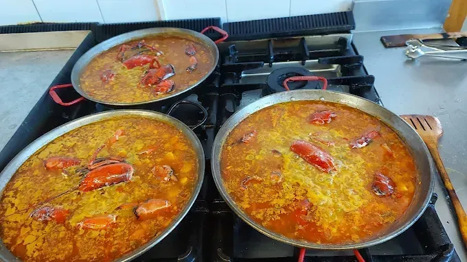 Tres sartenes de paella cocinándose en una estufa de gas, con pimientos rojos y arroz amarillo.