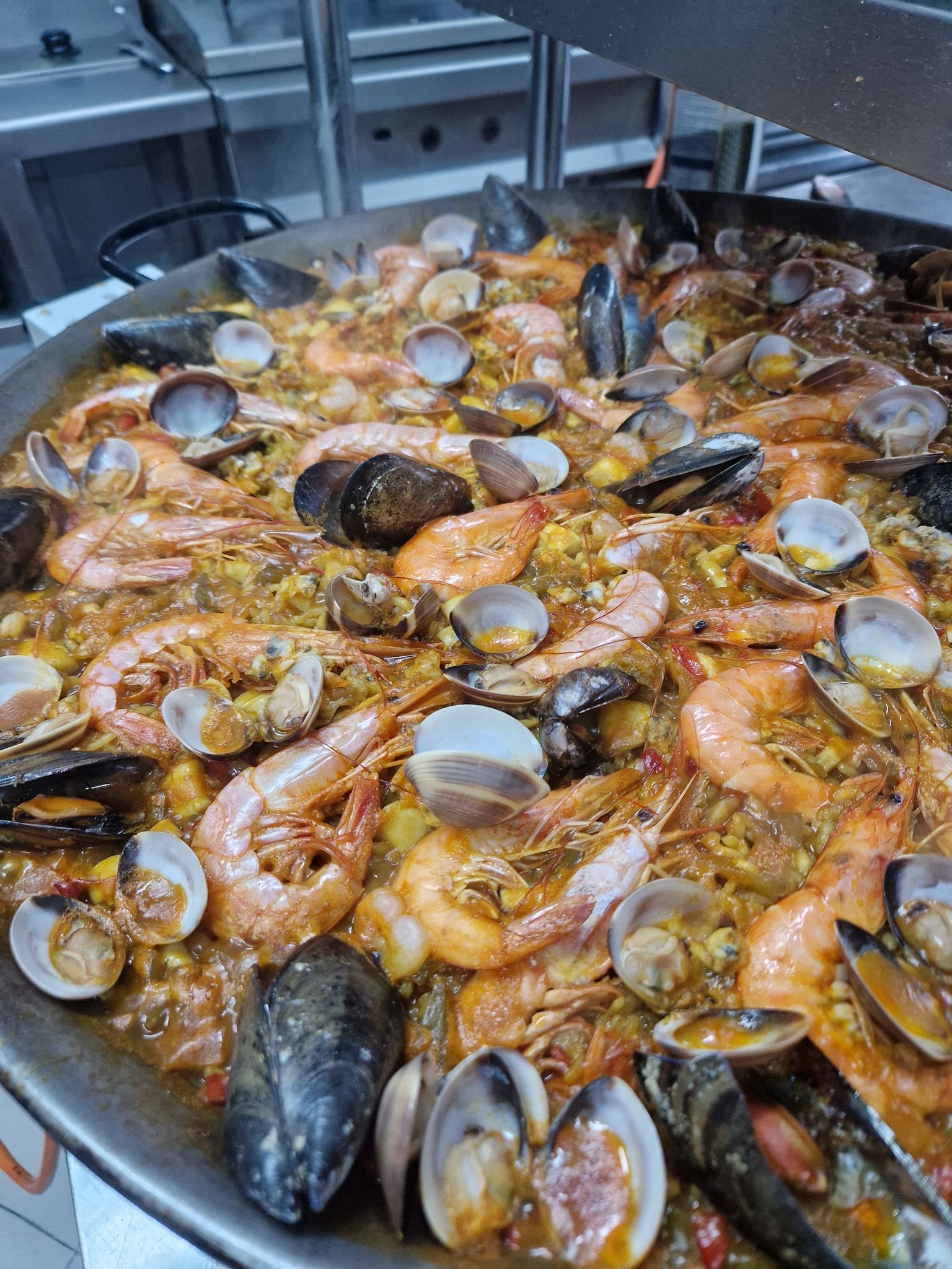Paella con camarones, mejillones y almejas en una sartén grande, humeante sobre la estufa.