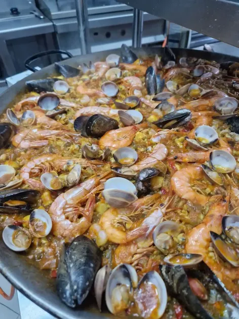 Paella con camarones, mejillones y almejas en una sartén grande, humeante sobre la estufa.
