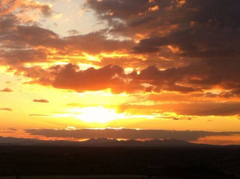 Puesta de sol de un intenso color naranja con nubes dramáticas sobre un horizonte oscuro.