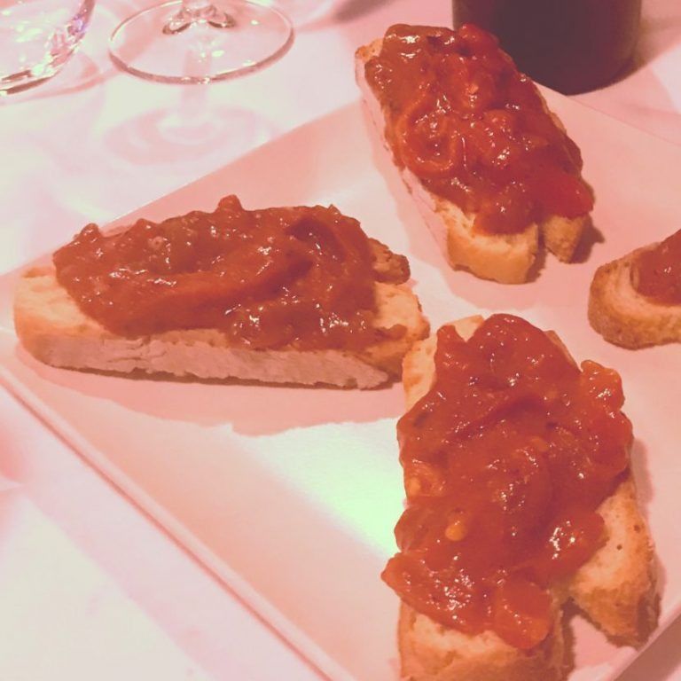 Bruschetta cubierta con salsa de tomate en un plato blanco bajo iluminación rosa.