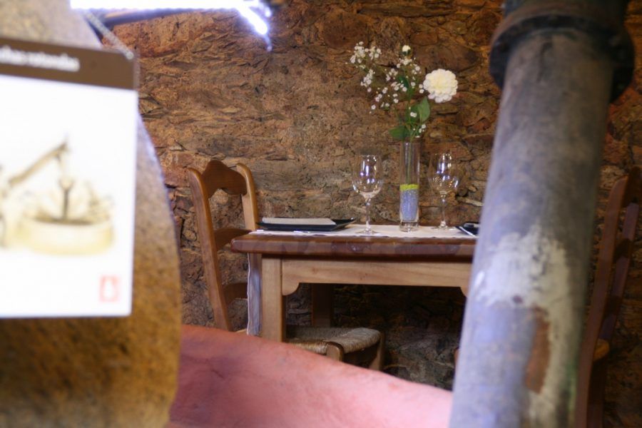 Acogedor rincón rústico para comer con mesa de madera, flores, copa de vino y paredes de piedra.