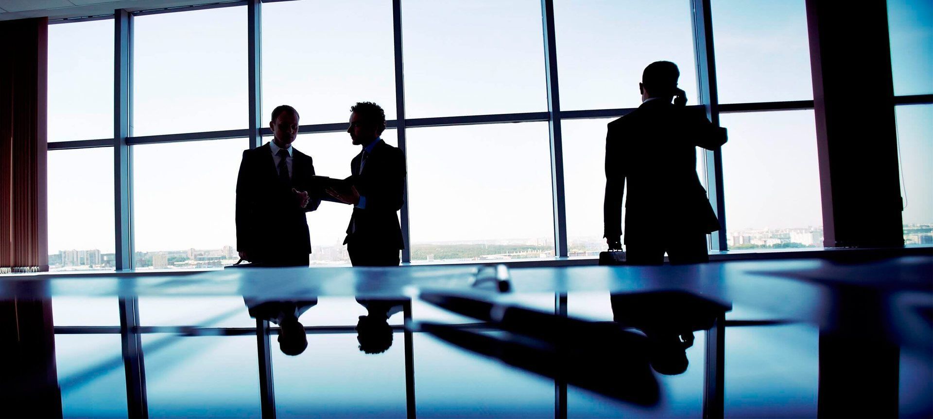 Un grupo de empresarios se dan la mano frente a una ventana.