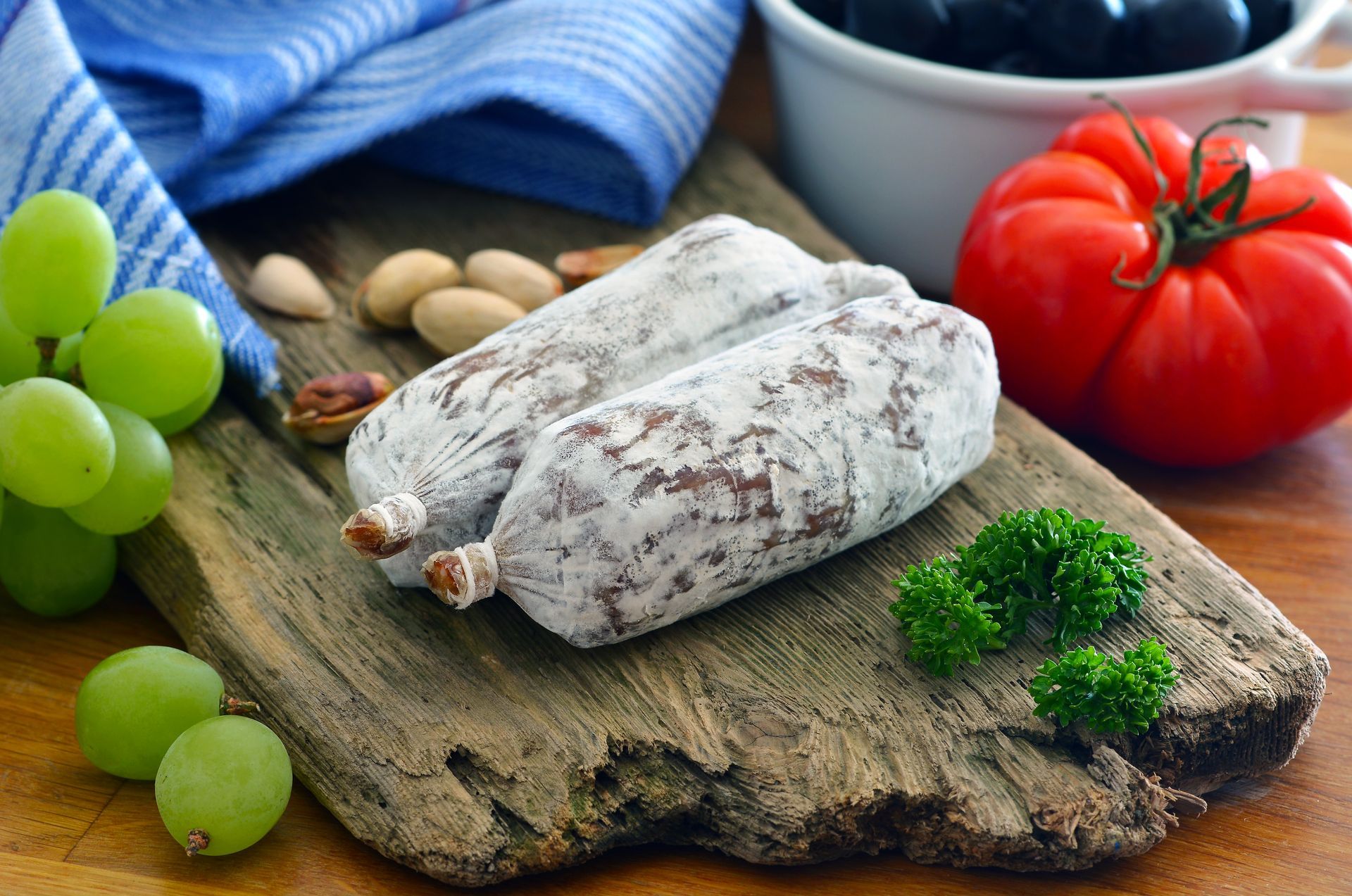 Un tagliere di legno con sopra salsiccia, uva, olive e prezzemolo. Osteria Teatro Unione L'Entrecôte 