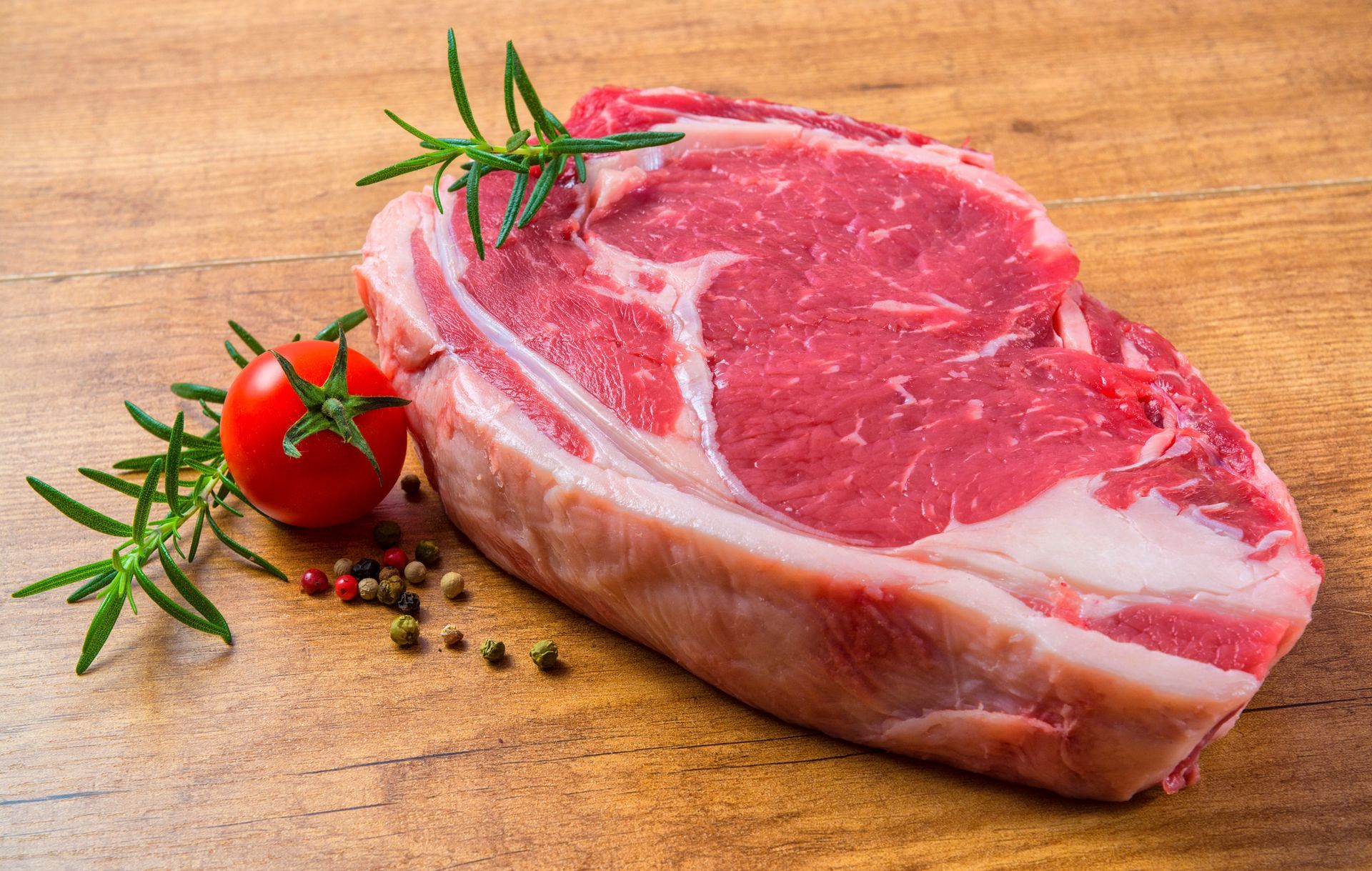 Una bistecca cruda è appoggiata su un tavolo di legno accanto a un pomodoro e del rosmarino. Osteria Teatro Unione L'Entrecôte 