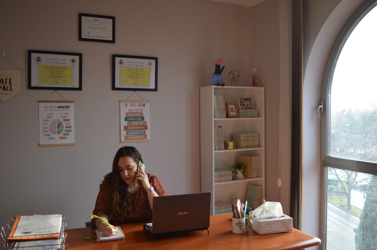 Una mujer está sentada en un escritorio con una computadora portátil y hablando por un teléfono celular.