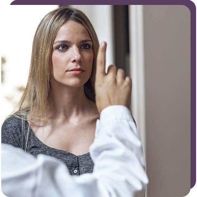 Mujer mirando hacia un dedo levantado. Persona con bata blanca extiende el dedo hacia ella, en un interior.