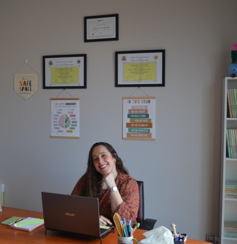 Una mujer se sienta en un escritorio frente a una computadora portátil.