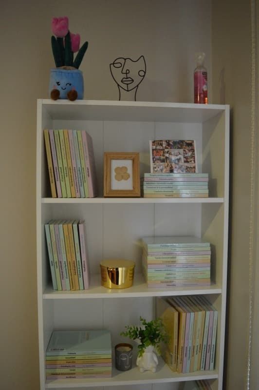 Una estantería blanca llena de libros, fotografías y un jarrón con flores.