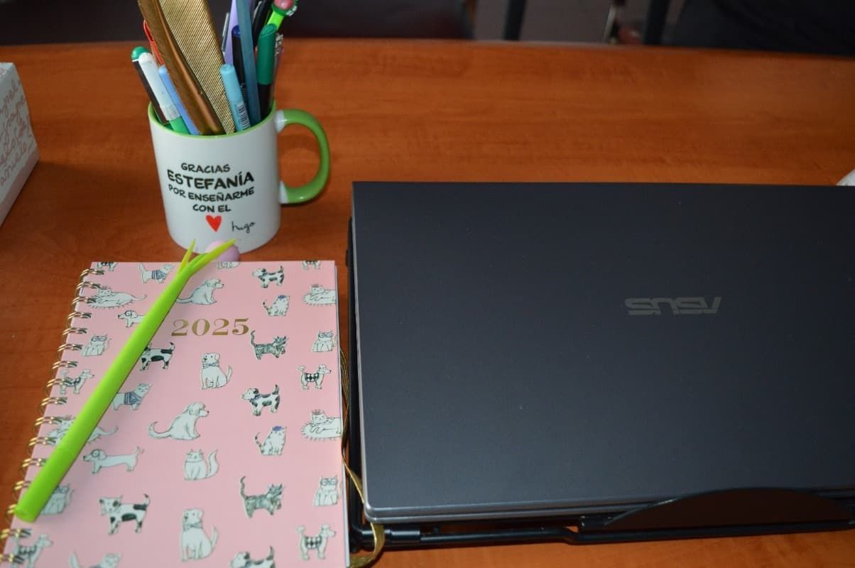 Una computadora portátil Asus se encuentra en un escritorio junto a una taza con bolígrafos.