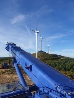 Una grúa azul está sentada en la cima de una colina con turbinas eólicas en el fondo.