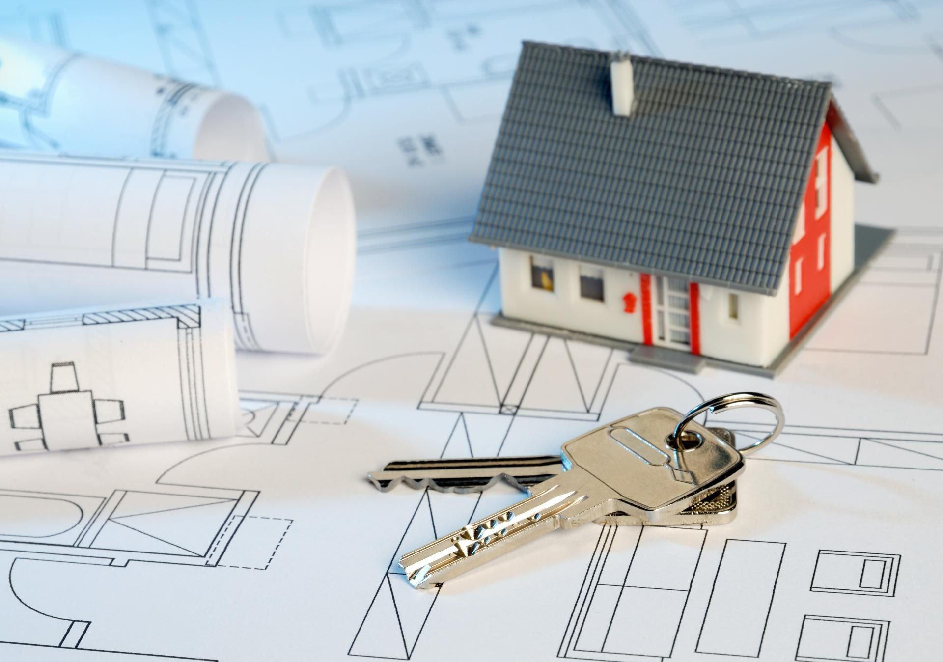 Ein Modellhaus steht auf einem Bauplan neben einem Schlüssel
