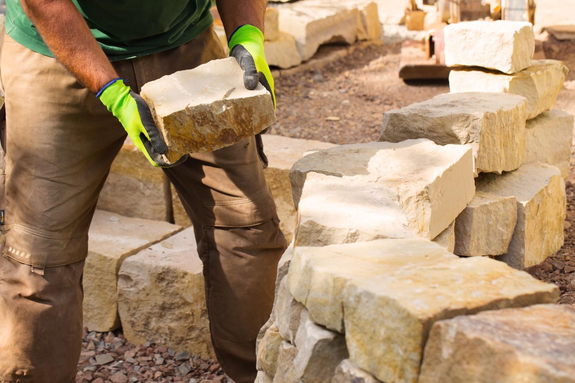 Ein Mann hält einen Ziegelstein in seinen Händen, während er an einer Steinmauer arbeitet.