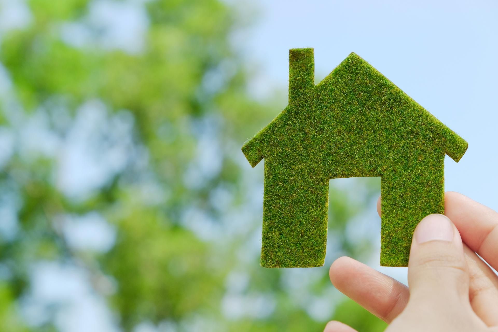 Eine Person hält ein Haus aus Gras.