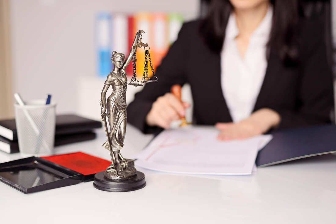 Una mujer está sentada en un escritorio con una estatua de la justicia.
