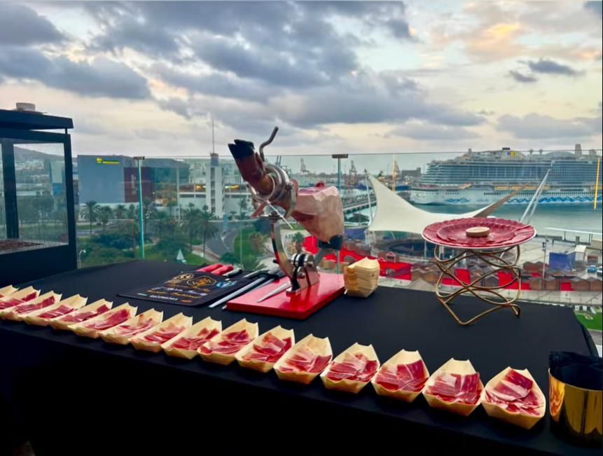 Estación de jamón curado en una azotea con vistas a la ciudad y al puerto al atardecer. 