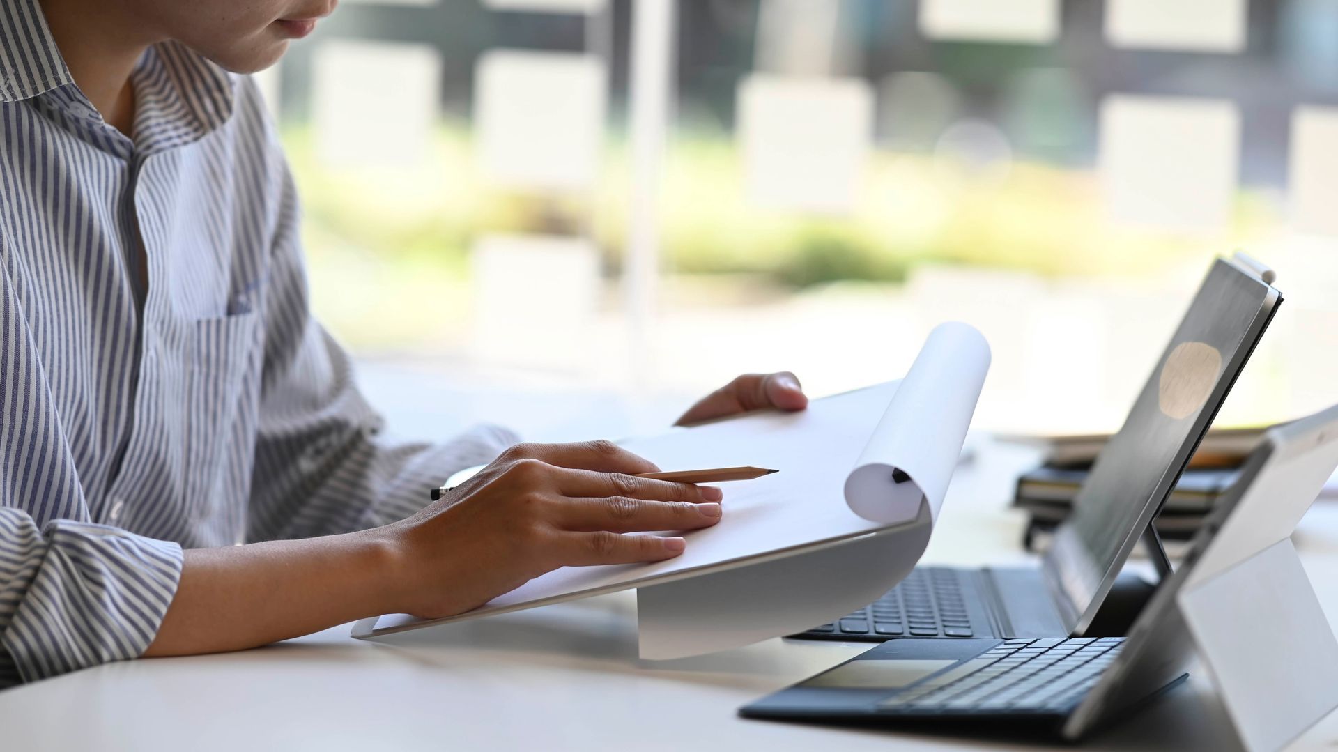 A man is sitting at a desk with a laptop and looking at a piece of paper.