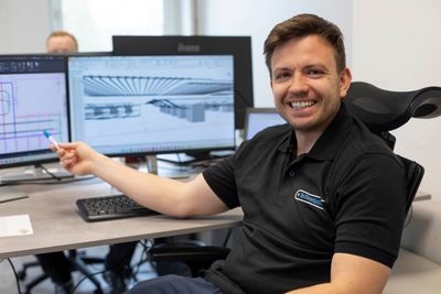 Ein Mann sitzt an einem Schreibtisch vor zwei Computermonitoren.