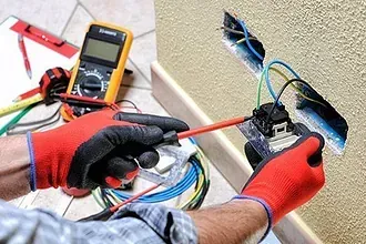 Un electricista está trabajando en una toma eléctrica con un destornillador.