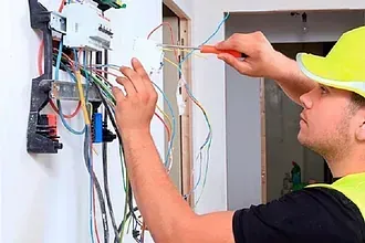 Un hombre está trabajando en una caja eléctrica con un destornillador.