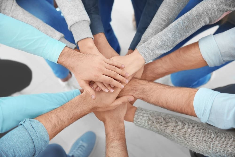 Eine Gruppe von Menschen legt ihre Hände zu einem Kreis zusammen.