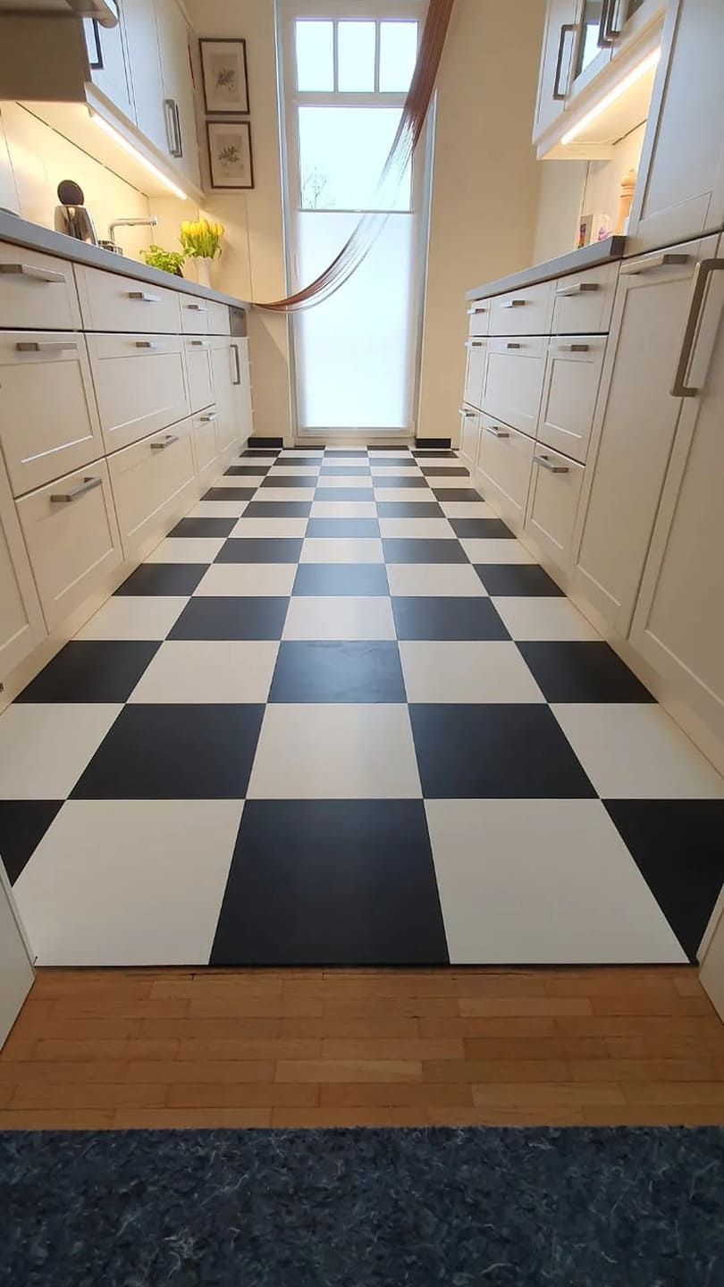 Ein schwarz-weiß karierter Boden in einer Küche mit weißen Schränken.