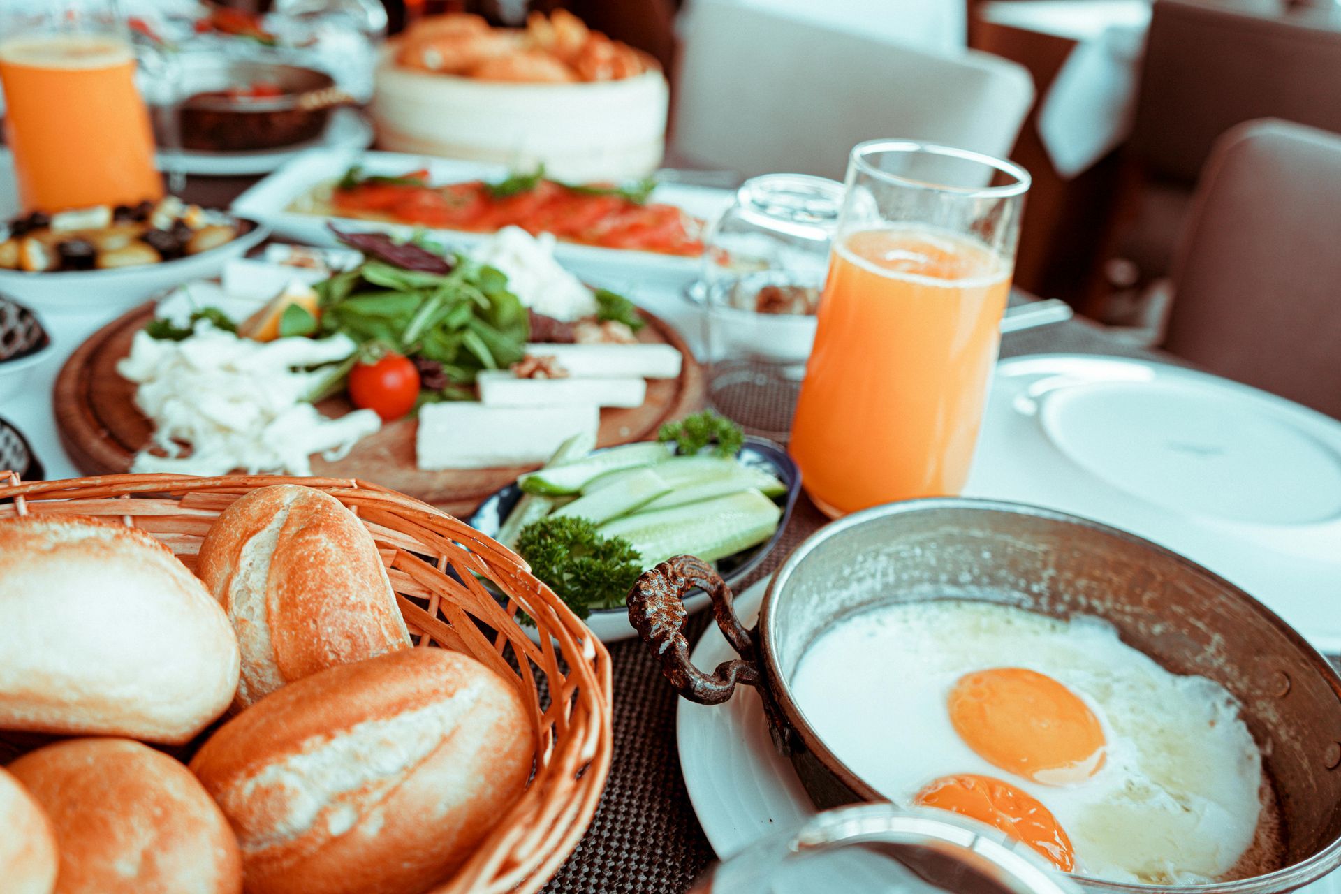 a spread of breakfast with orange juice, bread basket, and eggs