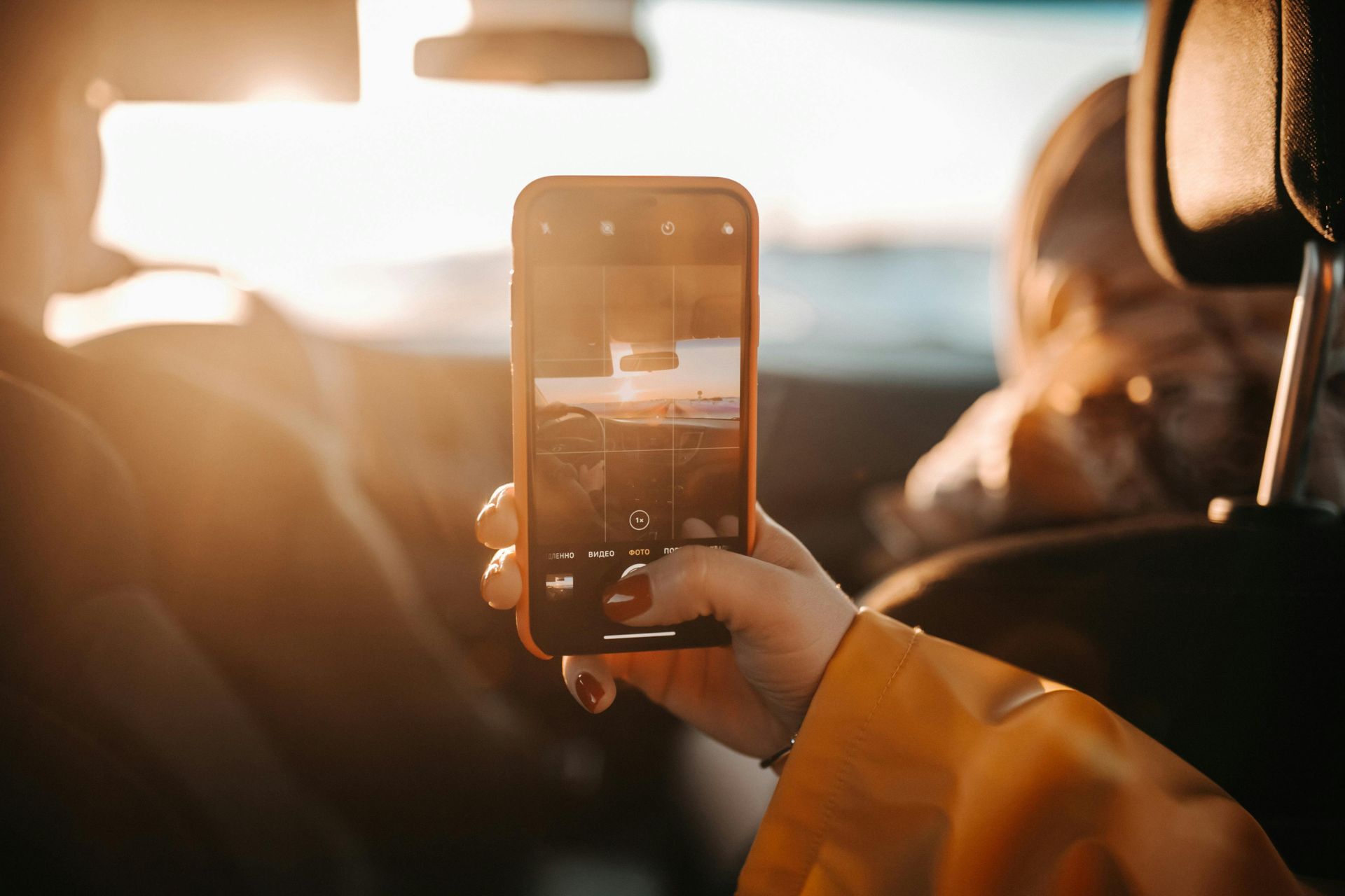 a person wearing nail paint taking picture of a sunset on their phone 