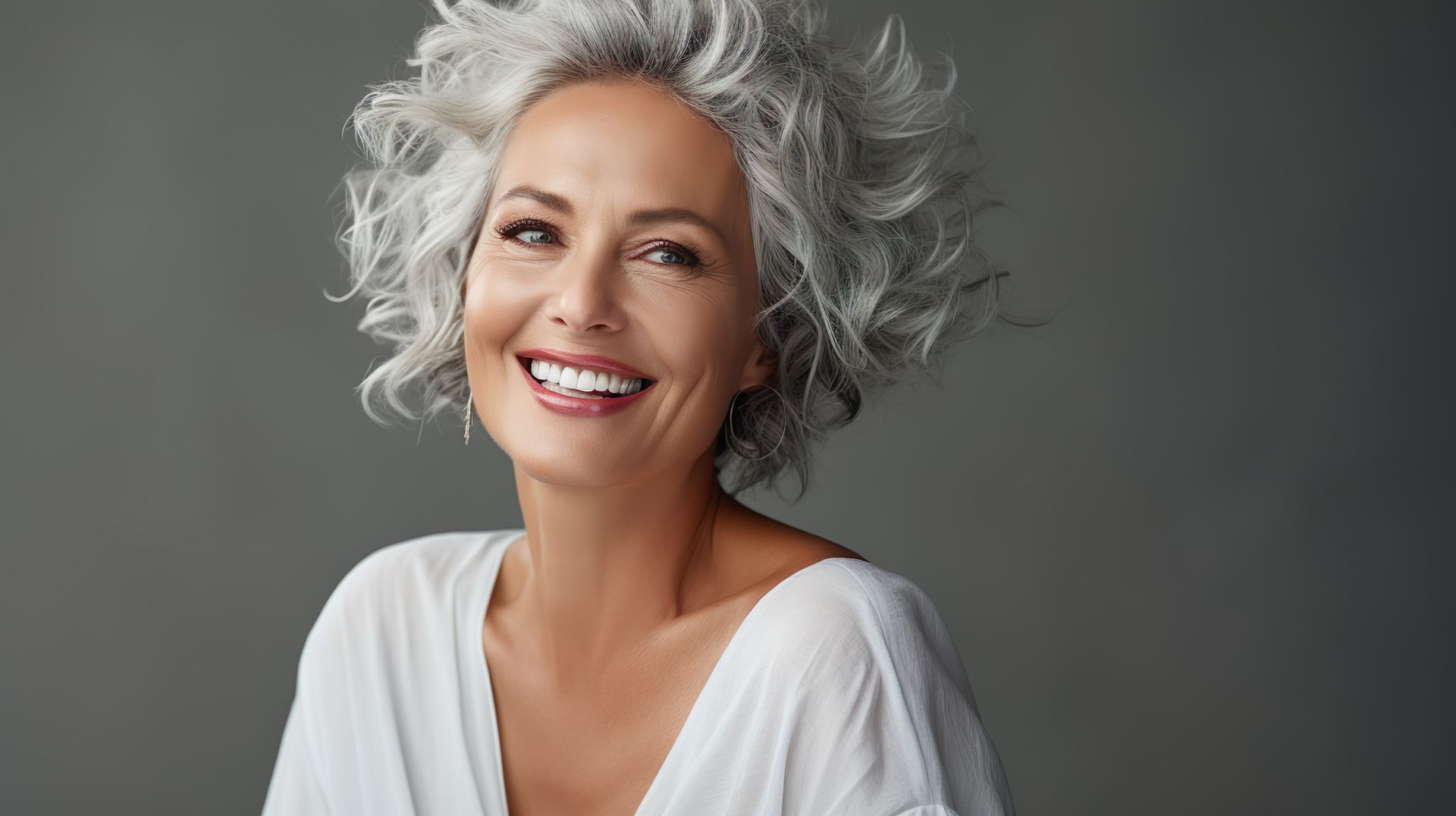 Eine Frau mit grauem Haar lächelt und trägt ein weißes Hemd.