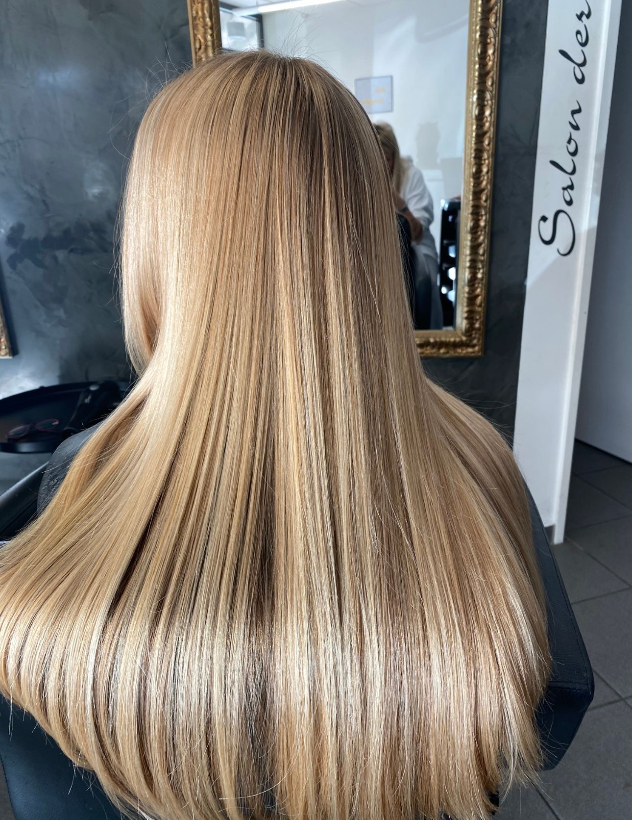 Eine Frau mit langen blonden Haaren sitzt in einem Salon vor einem Spiegel.