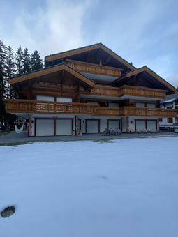 Sol enneigé devant un chalet de trois étages avec balcons et boiseries en bois.