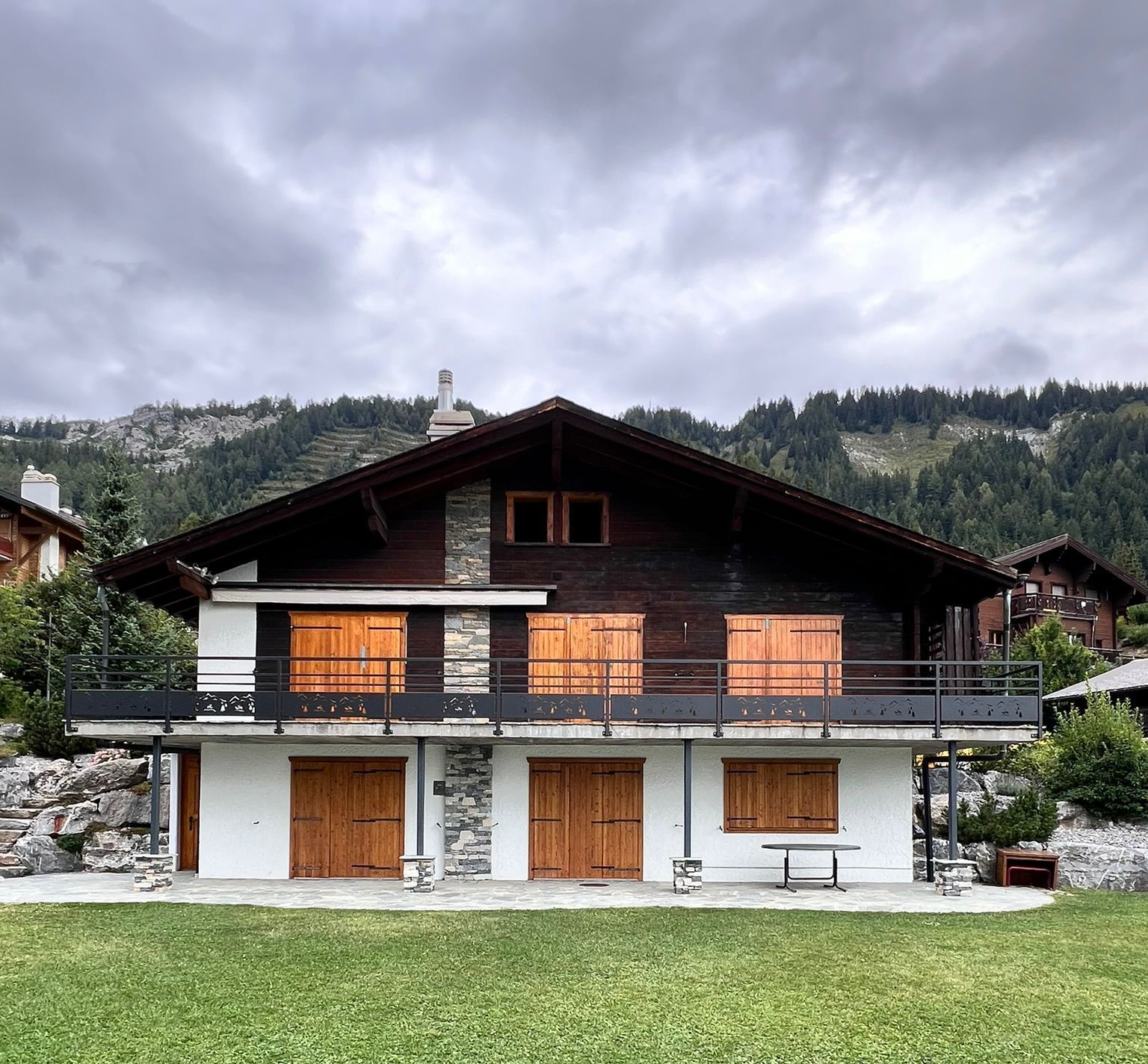 Chalet à deux étages avec un niveau inférieur blanc et un niveau supérieur en bois brun ; volets en bois ; pelouse verte,