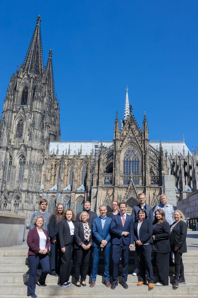 Eine Gruppe posiert vor dem Kölner Dom unter strahlend blauem Himmel