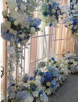 Structure florale blanche avec fleurs incluses, parfaite pour une décoration de mariage, un coin photo ou une table d’honneur. Disponible à la location au prix de 100,00 €.