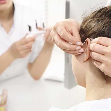 A una mujer le están colocando un audífono en el oído.