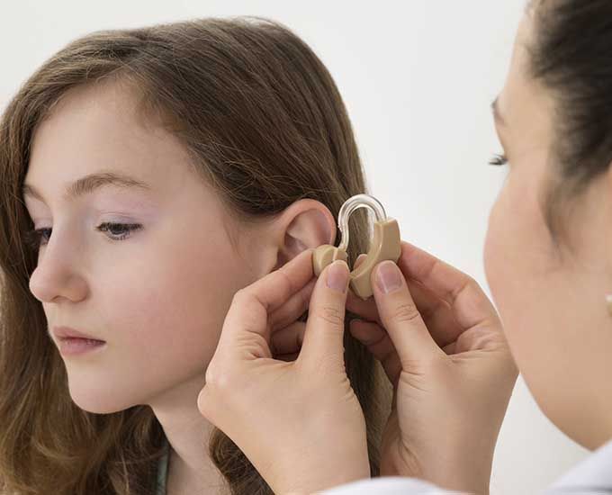 Una mujer está colocando un audífono en el oído de una niña.
