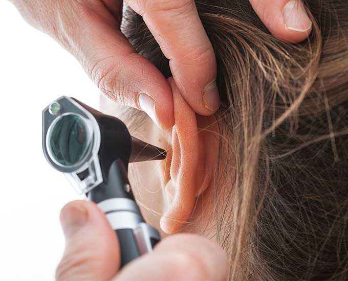 Un médico está examinando la oreja de una mujer con un otoscopio.