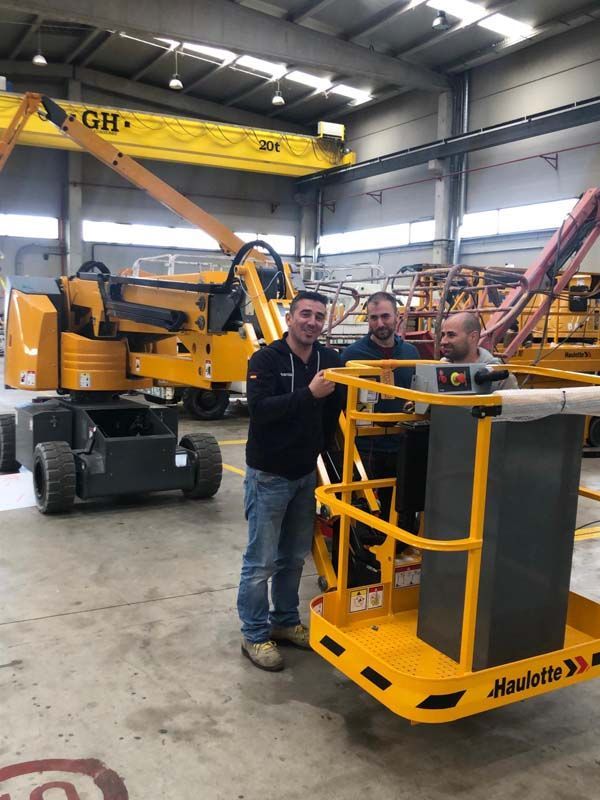 Tres hombres están parados frente a una máquina amarilla que dice 'Haulotte'.