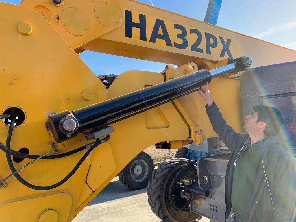 Un hombre está ajustando un cilindro hidráulico en un tractor amarillo.