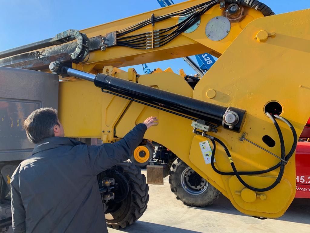 Un hombre está de pie junto a un gran tractor amarillo.