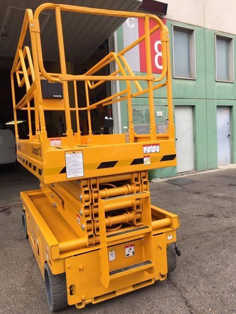 Un elevador de tijera amarillo está estacionado frente a un edificio con el número 3.