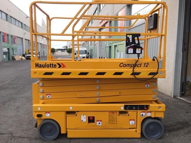 Un elevador de tijera Haulotte Compact 12 amarillo está estacionado en un estacionamiento