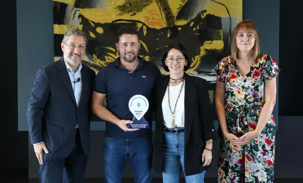 Cuatro personas posando en interiores, una de ellas sosteniendo una pequeña placa de premio