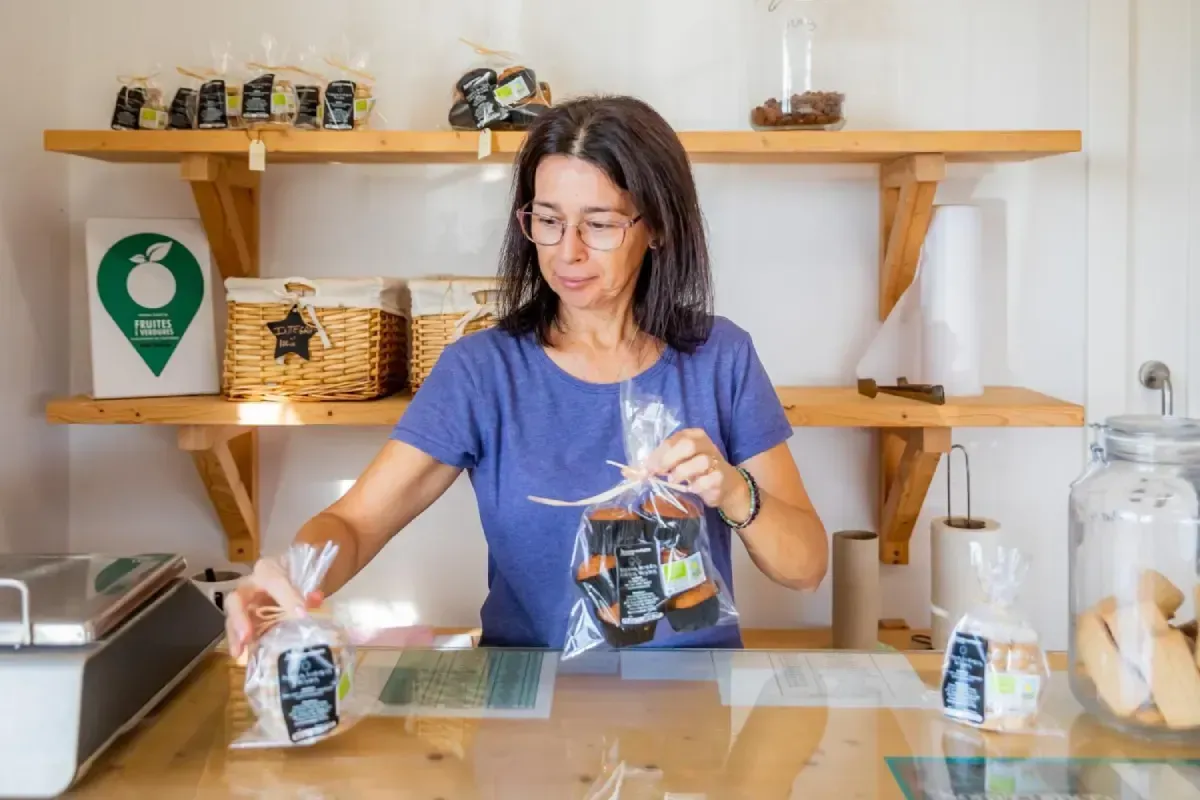 Una mujer empaca una bolsa reutilizable en la encimera de la cocina, con estantes y frascos al fondo.
